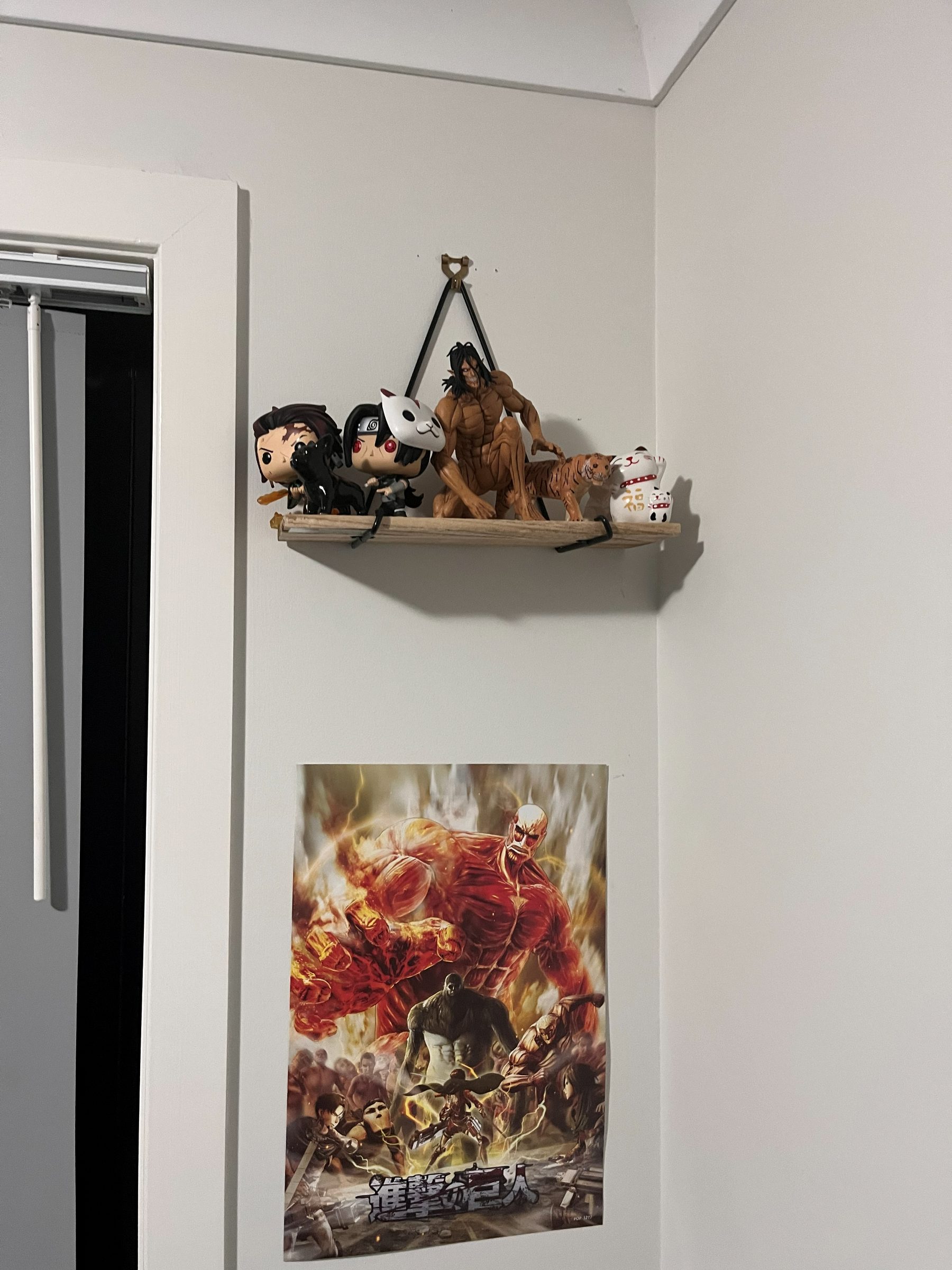 A small hanging shelf holding Tanjiro and Itachi figures, an Attack on Titan Eren figure, a tiger and a lucky cat, with an Attack on Titan poster on the wall below