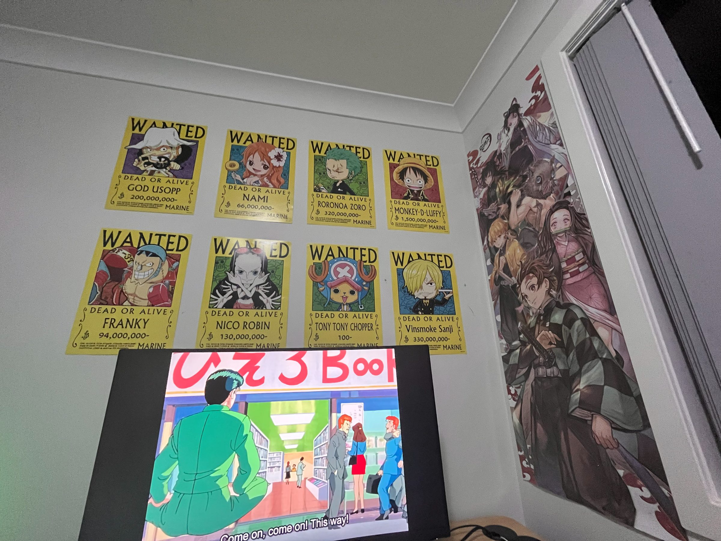 A bedroom corner with eight One Piece wanted posters across one wall, a Demon Slayer poster on the next, and Yu Yu Hakusho playing on a projector screen below