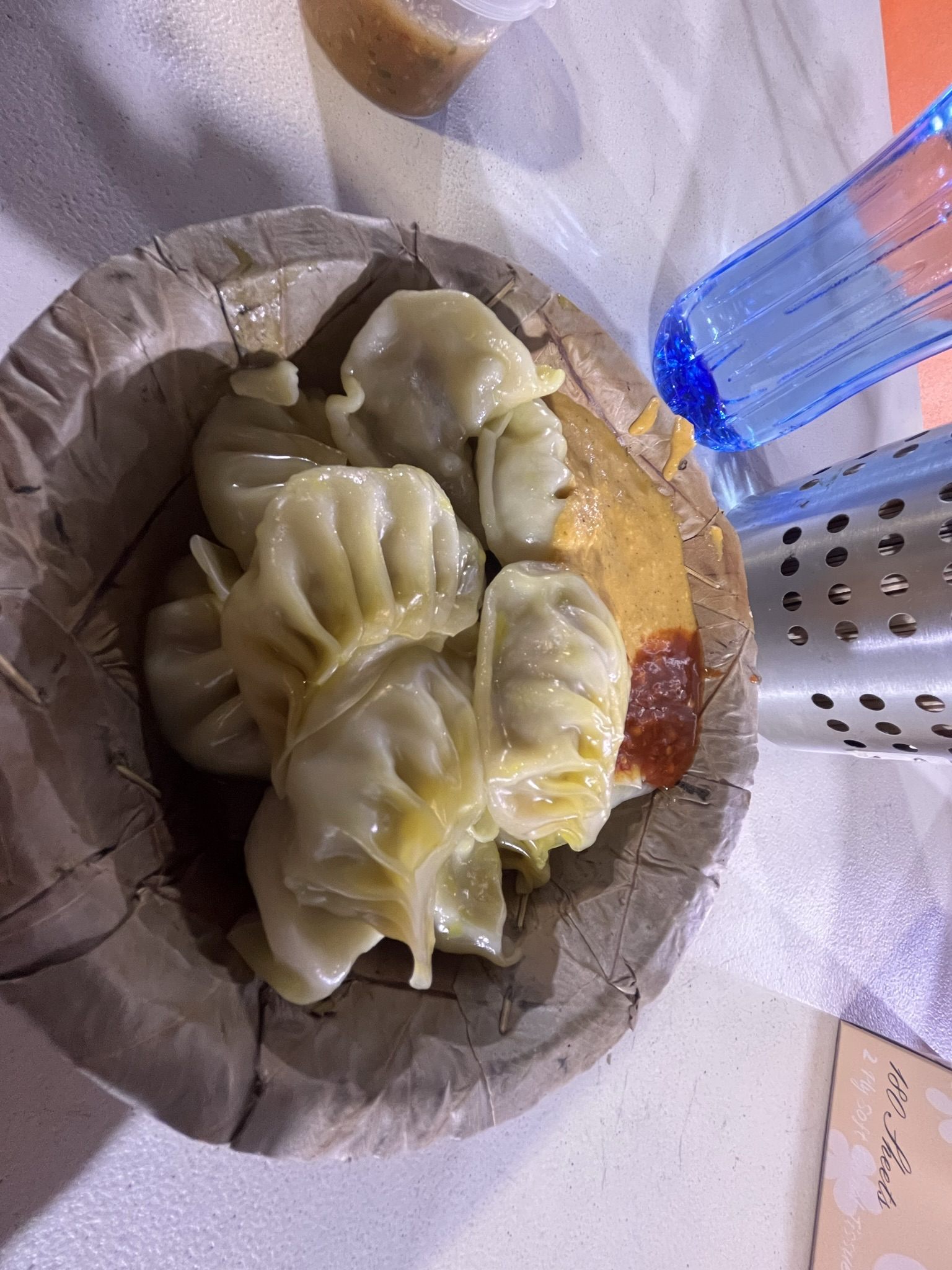 Steamed momo in a pressed-leaf bowl with two chilli sauces beside them, on a white table
