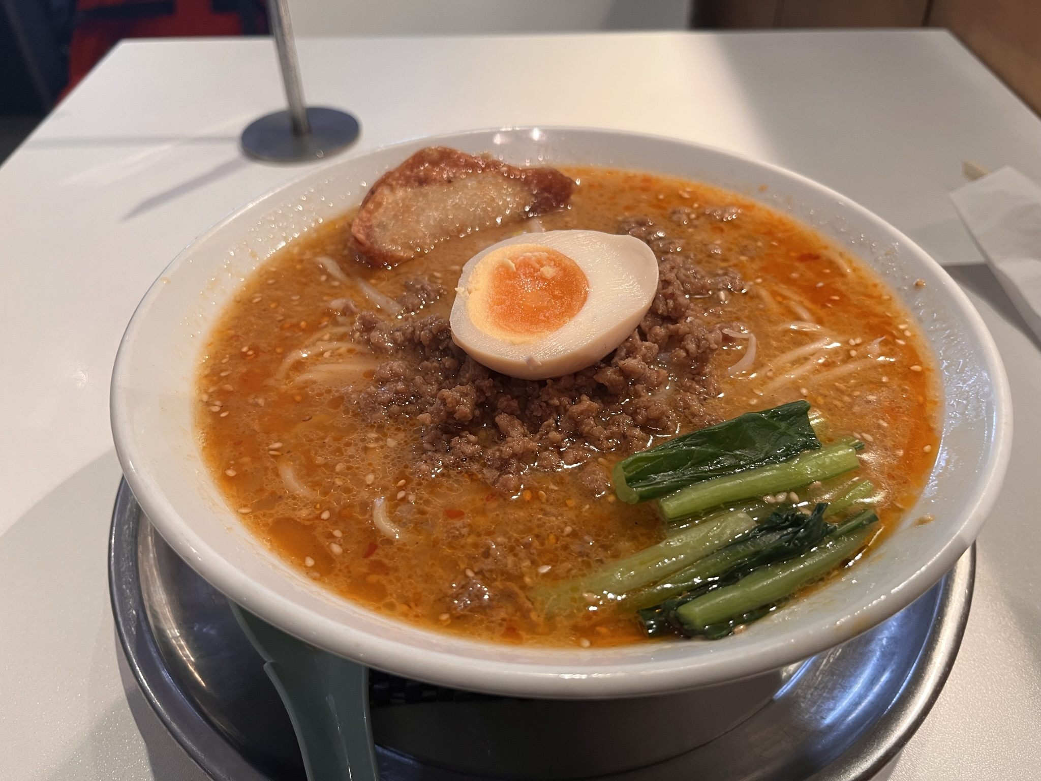 A white bowl of spicy sesame ramen with minced pork, pak choi and half a marinated egg