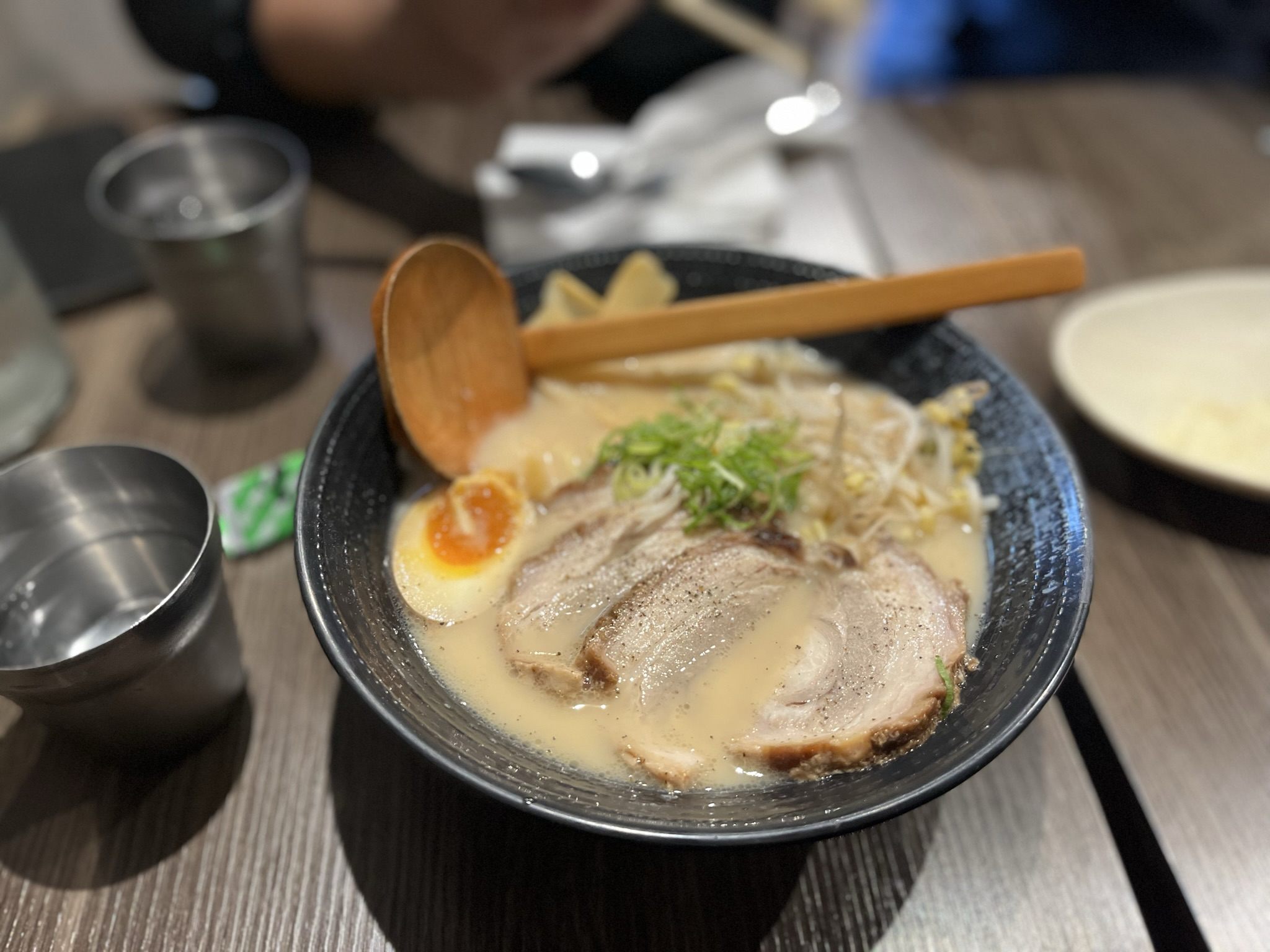 Tonkotsu ramen with chashu, bean sprouts and half a marinated egg, a wooden ladle resting across the bowl