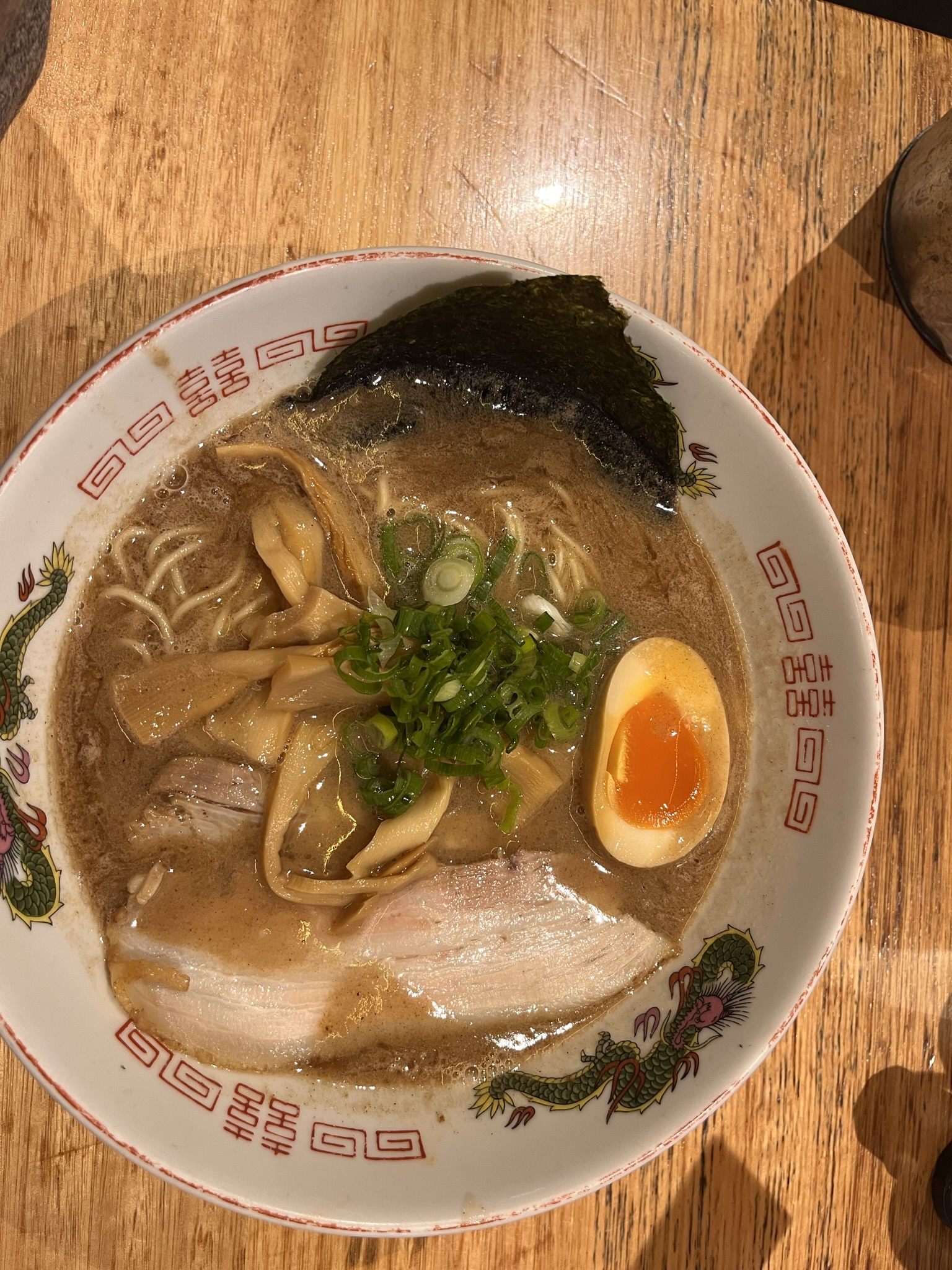 A dragon-patterned bowl of ramen photographed from above — chashu, bamboo shoots, nori, spring onion and a halved marinated egg